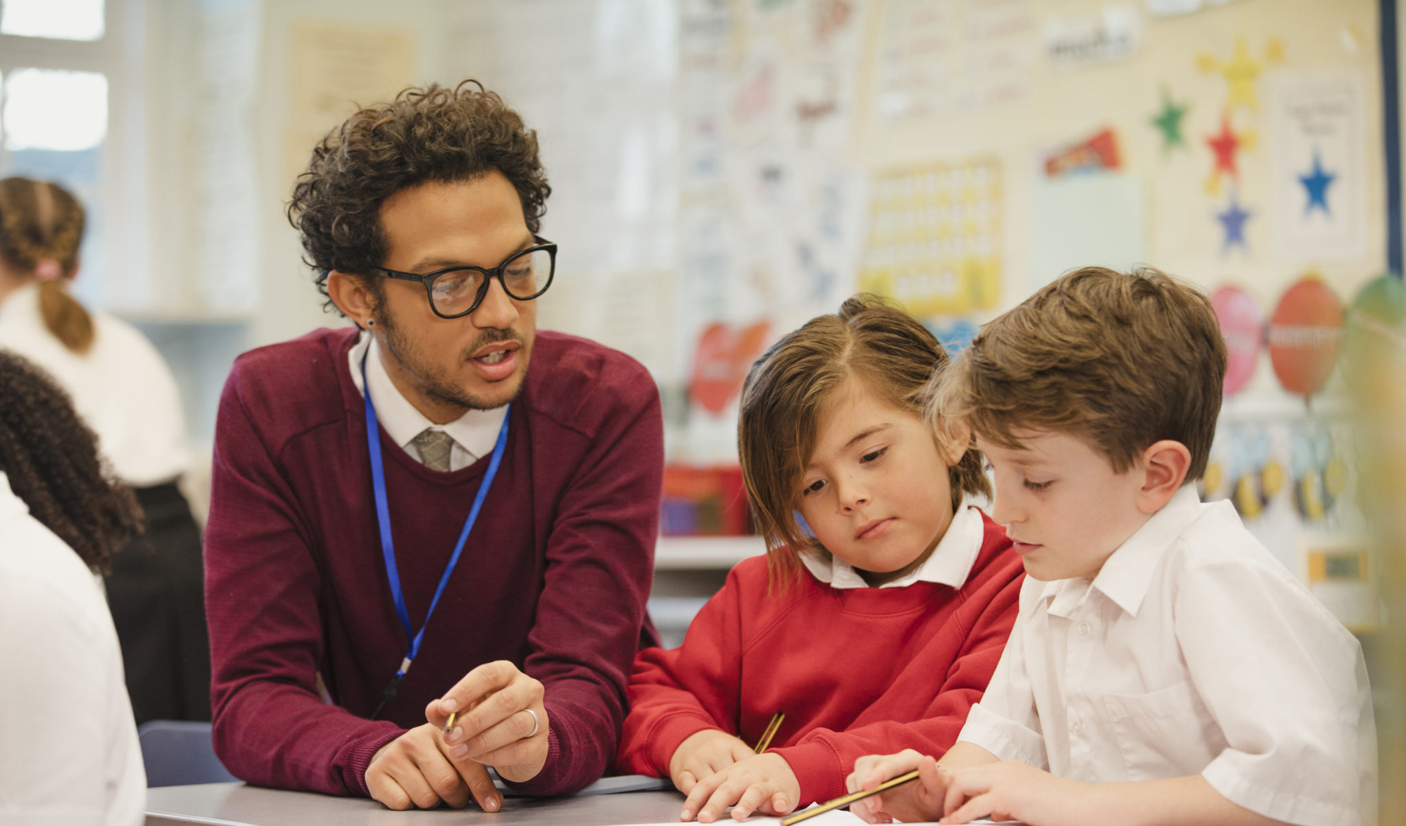 Two schoolboys work through a textbook with their teacher in elementary class. This is a school in Hexham, Northumberland in north eastern England.