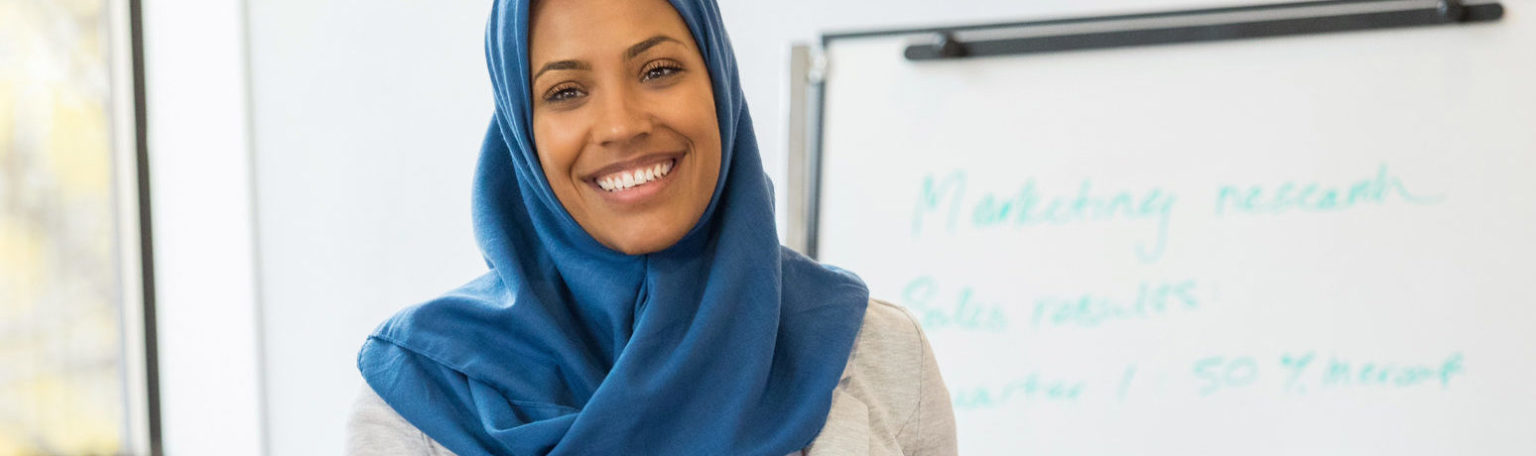 A mid adult Muslim businesswoman smiles as she speaks to a group of employees during a training class.